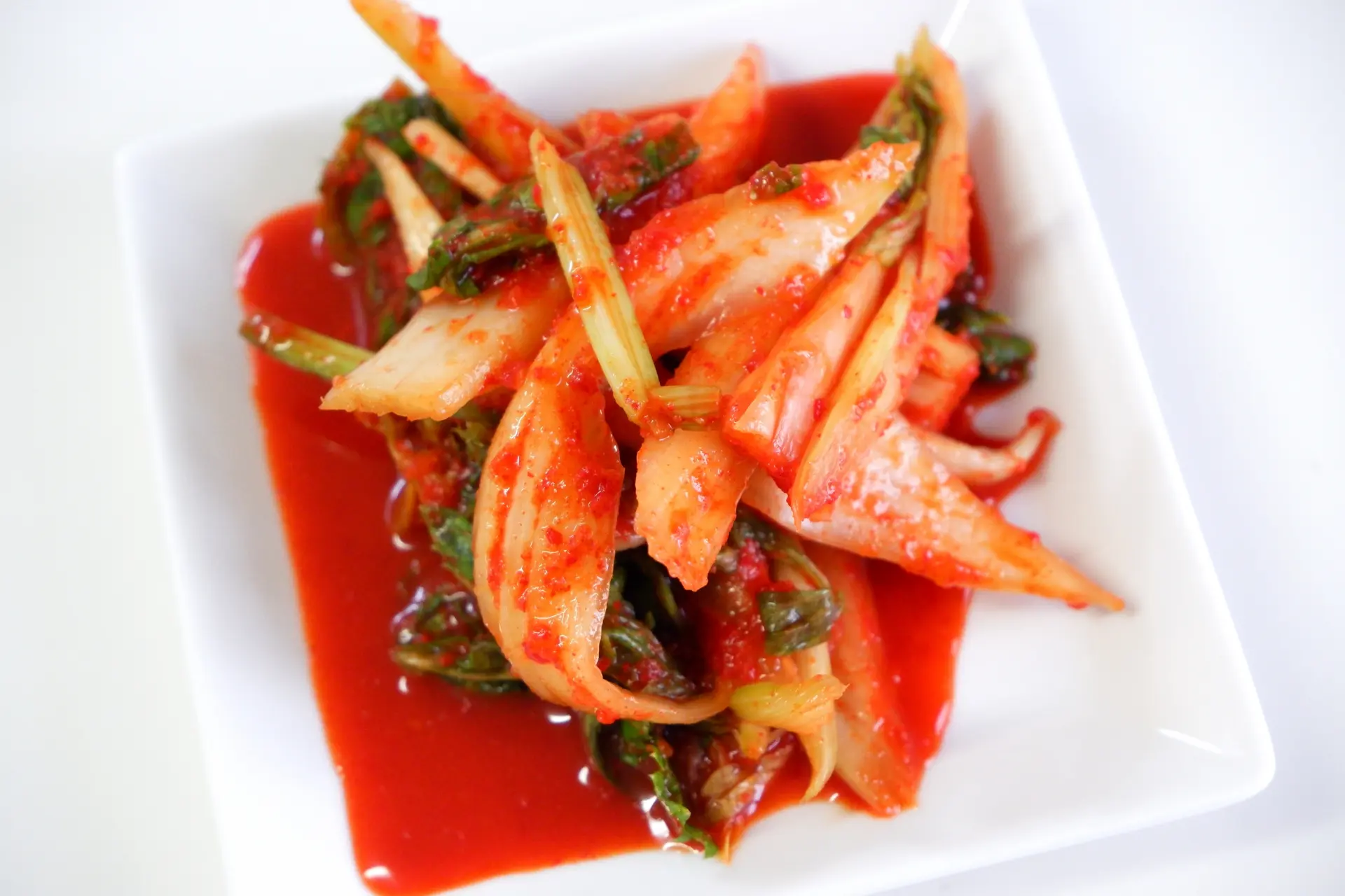 A plate of red spicy Celery Kimchi on a white table